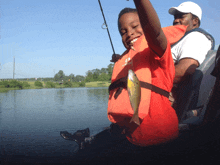 a boy wearing an orange life vest is holding a fish in his hand