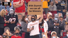 a man in a stormx shirt holds up a sign