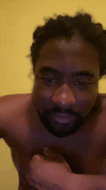 a shirtless man with a beard and dreadlocks looks at the camera