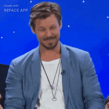 a man with a beard is wearing a blue jacket and a white shirt and a necklace .