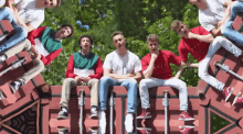 a group of young men are sitting on top of a brick wall with the letter e visible in the background