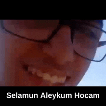 a close up of a person wearing glasses and smiling with the words selamun aleykum hocam below them .