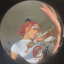 a woman with red hair is taking a selfie with a fisheye lens while wearing a mario shirt .