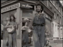 a group of people are standing in front of a store . one of the men is playing a banjo .