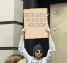 a man holding a sign that says give me my money hodge