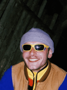 a young man wearing sunglasses and a beanie smiles for the camera