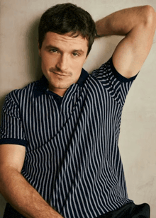 a man wearing a blue and white striped polo shirt with his hand behind his head