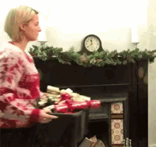 a woman is holding a box of christmas crackers in front of a fireplace with a clock in the background