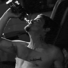 a black and white photo of a shirtless man drinking water