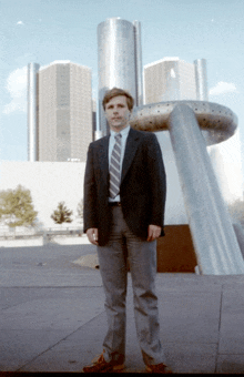 a man in a suit and tie stands in front of a large sculpture