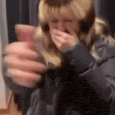 a woman is holding a glass of wine and covering her mouth with her hand .