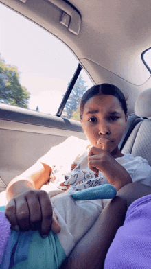 a little girl is sitting in the back seat of a car eating a snack