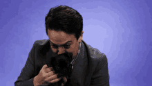 a man in a suit is holding a small black dog in his hands