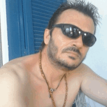 a shirtless man wearing sunglasses and a necklace looks at the camera .