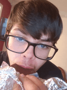 a young man wearing glasses is eating a chocolate bar