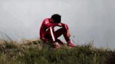 a man in a red outfit sits on a grassy hill with his head down