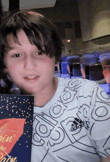 a boy in an adidas shirt holds a book