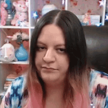 a woman with pink hair is sitting in a chair in front of a shelf with stuffed animals on it .