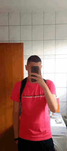 a man in a pink shirt is taking a selfie in front of a mirror