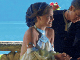 a woman in a white dress with a blue necklace is sitting next to a man
