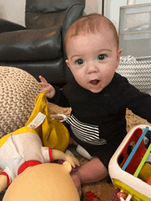 a baby wearing a black and white striped shirt is sitting on the floor with toys