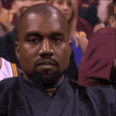 a man with a beard is sitting in a crowd of people and making a funny face .