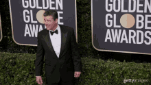 a man in a tuxedo walks on a red carpet in front of a sign that says golden globe awards