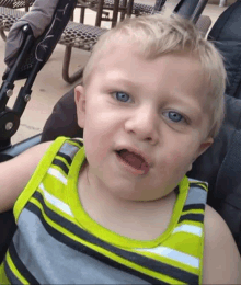 a young boy with blue eyes is sitting in a stroller with his mouth open