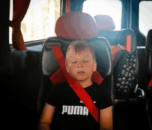 a boy wearing a black puma shirt is sleeping in a car seat