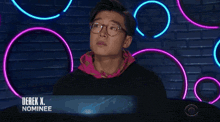 a man with glasses is sitting in front of a neon sign that says derek nominee