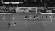 a black and white photo of a soccer game on a field with advertisements on the sidelines .