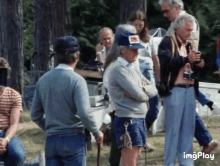 a group of people are standing in a field and one man is wearing a hat that says ' ford ' on it