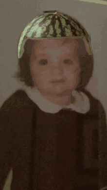 a little girl wearing a watermelon hat looks at the camera