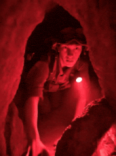 a man wearing goggles and a helmet is crawling through a cave