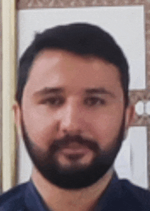 a man with a beard and a blue shirt is standing in front of a wall .