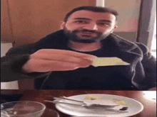 a man with a beard is sitting at a table eating a piece of cheese .