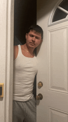 a man in a white tank top stands in front of a door