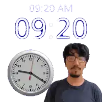 a man wearing glasses stands in front of a clock that reads 9:20 am