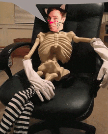 a man in a cat costume sits in a chair with a skeleton behind him