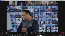 a man stands in front of a wall of people on a zoom call