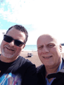 two men are posing for a picture on a beach with a lifeguard tower in the background