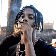 a man with dreadlocks is smoking a cigarette in front of a tree