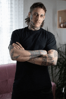 a man with a lot of tattoos on his face and arms stands with his arms crossed