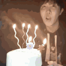 a man blows out candles on a cake with a flower on it