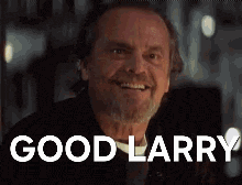 a man with a beard is smiling and the words `` good larry '' are on the screen behind him .