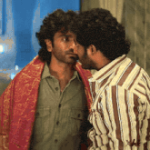 a man in a striped shirt is kissing another man in a green shirt