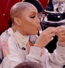 a woman wearing a pearl necklace and hoop earrings is sitting at a table eating a piece of food .