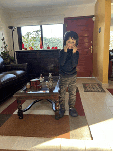 a young boy covering his face with his hands in front of a table