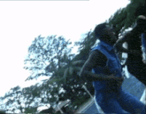 a man in a blue vest is dancing in front of a tree