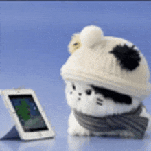 a stuffed animal wearing a hat and scarf looks at a cell phone